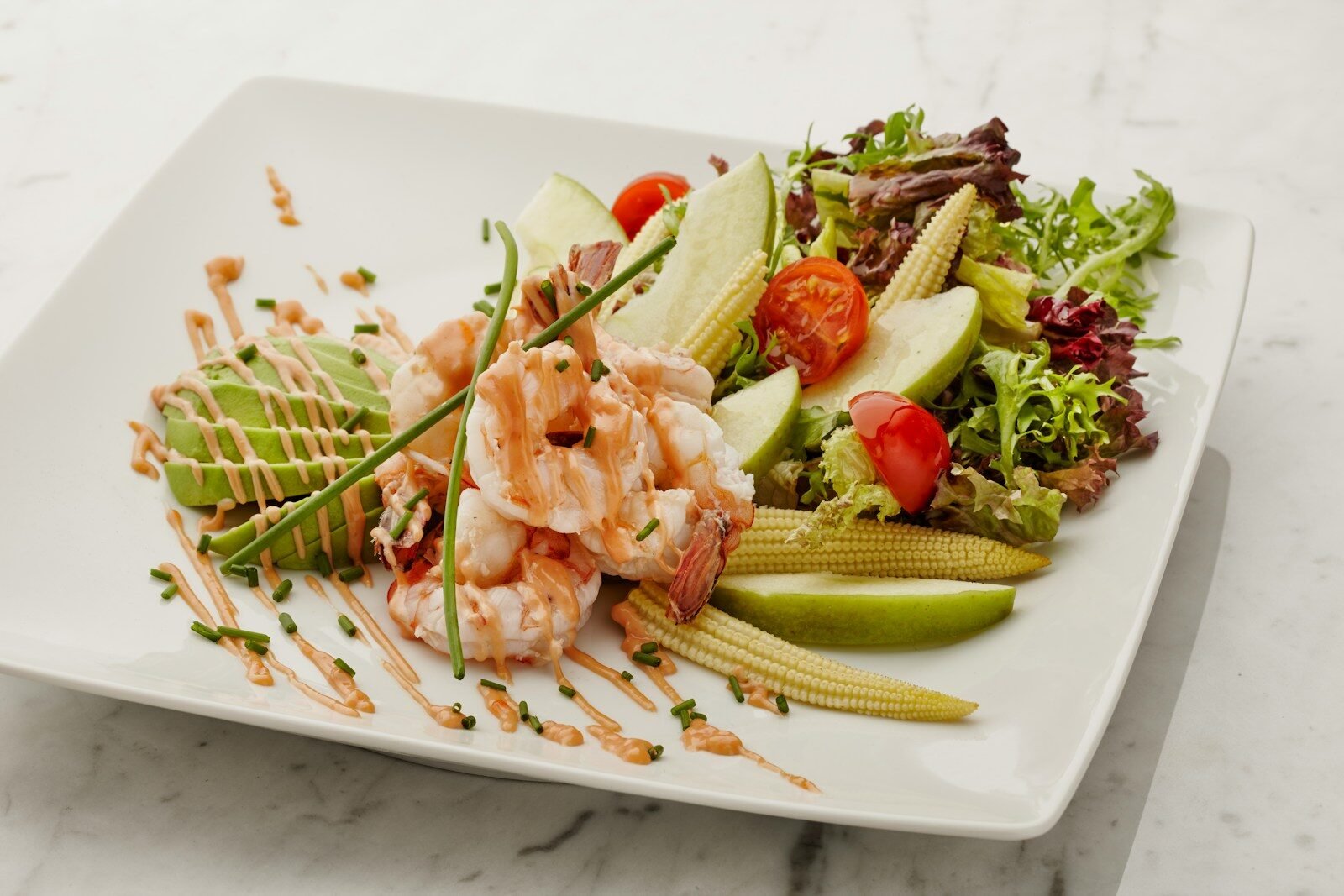 a white plate topped with a salad covered in shrimp